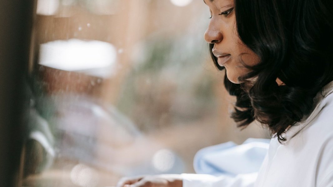 A Black woman writing her thoughts in a notebook at home.