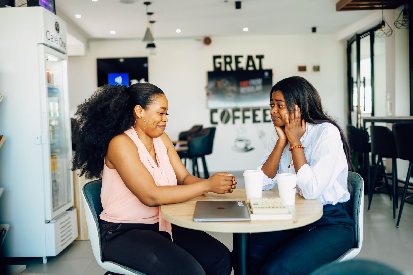 Two Black women sharing an honest conversation at a coffee shop.