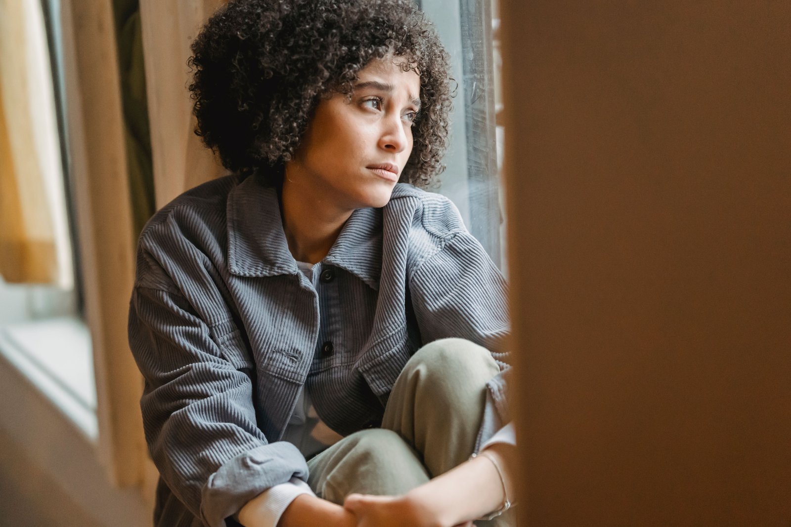 Black woman reflecting quietly while sitting near a window.