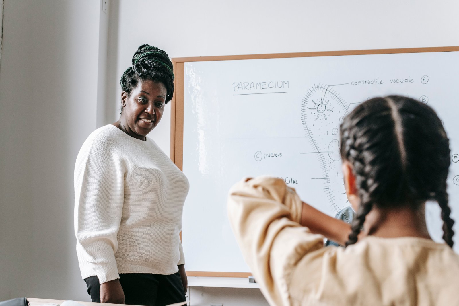 Black teacher speaking with a Black female student in a classroom.