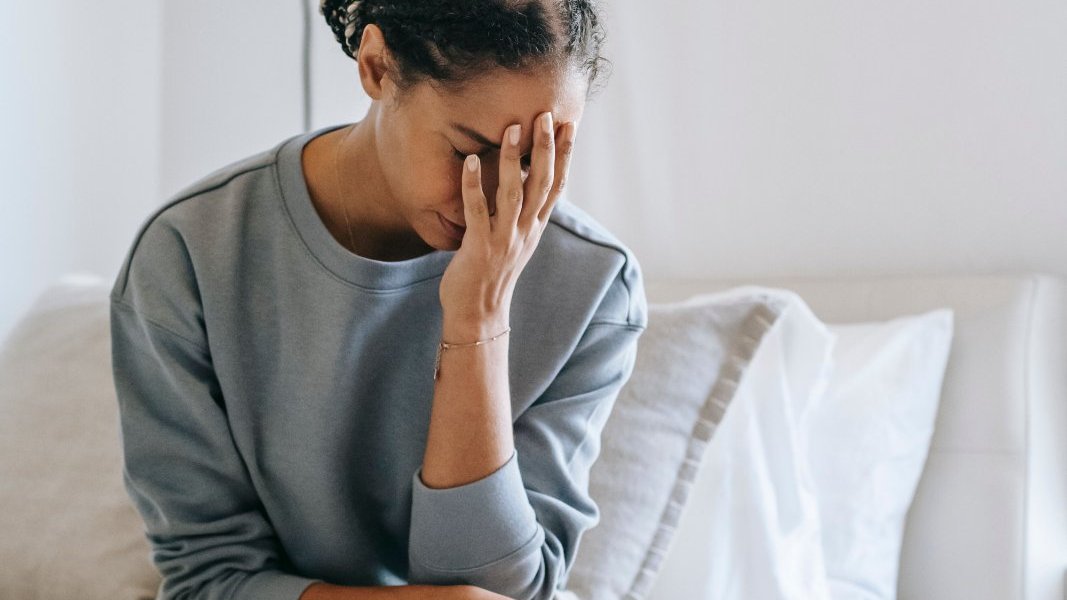 A Black woman in a calm home setting takes a moment for a gentle stretch, focusing on her well-being.